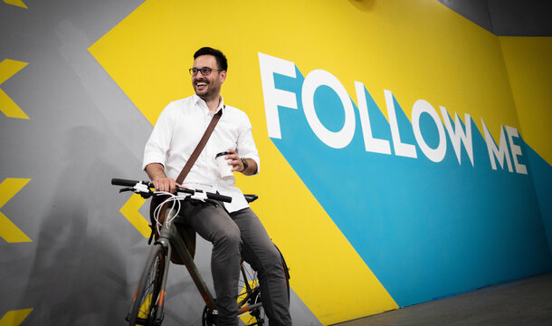 Business Man Sitting On Bike Near Wall With A Sign Follow Me