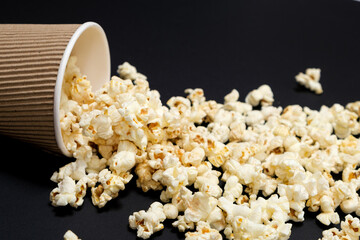 Popcorn spills out of a brown paper cup on a black background close-up