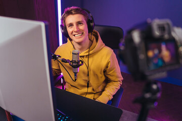 Happy young streamer pro gamer in headphones enjoying shooting vlog, smiling on camera, using microphone. Man pro gamer influencer streaming while playing computer video games. Esport and cyber sport © Arsenii
