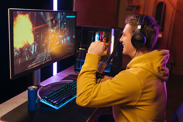 Side view of young caucasian pro gamer celebrating his victory in online video shooter game...