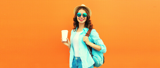 Portrait of happy smiling young woman with coffee cup wearing summer straw hat and backpack on orange background, blank copy space for advertising text