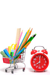 Shopping cart full school supplies and office supplies and red alarm clock white background.