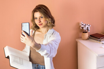 Portrait of attractive Young Vlogger woman filming book review on her smartphone. Cute girl Recording video blog