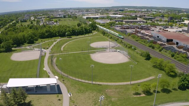 Aerial view of commuter train passes by an empty baseball diamond on a sunny summer day.
