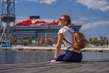 Woman traveler in the Port Vell  with large Virgin cruise liner on the background. Barcelona, Spain - May 29, 2022