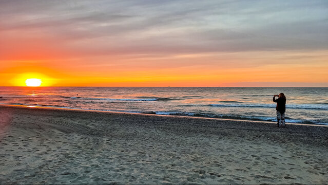 Eine einsame Person macht einen Schnappschuss vom Sonnenuntergang mit der Fotofunktion des Smartphones . Orange colored sky with ocean horizon and tiny waves .