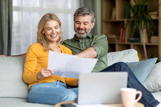 Family Insurance Concept. Happy Middle Aged Couple Reading Documents At Home