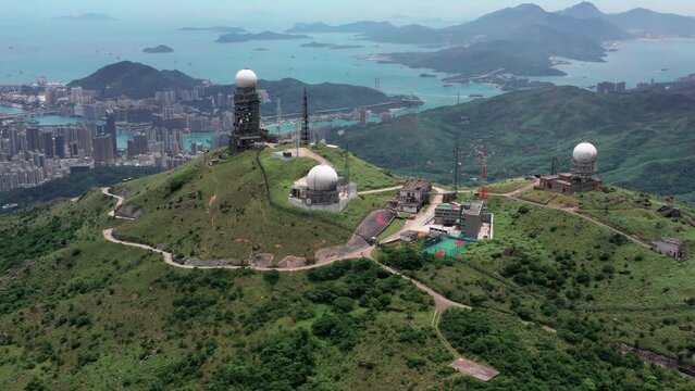 Aerial view of Sun rising at the tallest mountain Tai Mo Shan in Hong Kong with colorful blue sea and tall skyscrapers in the background.