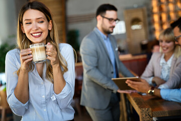 Portrait of happy young business woman drinking coffee in a break. In the background, her colleagues