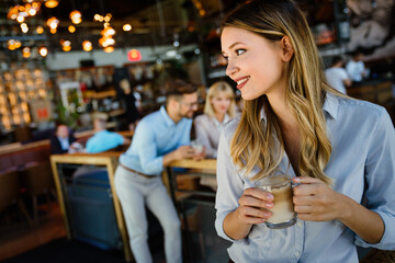 Portrait of happy young business woman drinking coffee in a break. In the background, her colleagues