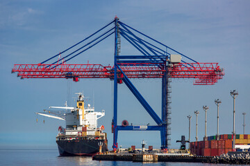 Obraz premium Cargo ship moored at the berth of the container ship yard for loading cargo by large cranes for unloading goods, cargo transportation by sea, shipping industry background.