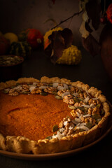 Musk gourd pie garnished with seeds, almond petals and walnuts, autumn table with pumpkins, dried flowers in a vase and a pie