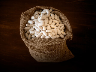 Dried white beans in a sack against a dark background