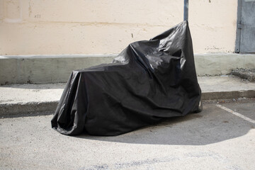 a rare motorcycle is hidden from prying eyes by a black cover next to a disabled sign in the parking lot near the house