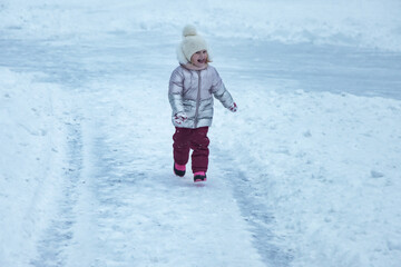 Fototapeta na wymiar Happy little girl in winter snowy public park walking in warm clothes
