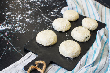 Board with uncooked cottage cheese pancakes and ingredients on black background
