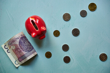 czerwona świnka skarbonka, monety i banknot na niebieskim tle 