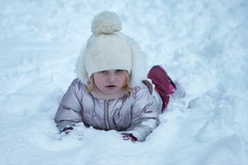 Fototapeta na wymiar Winter portrait happy little girl in snowy public park in warm clothes