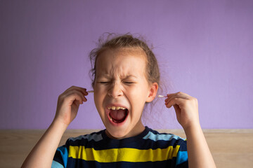 girl child in a striped turtleneck shows pain due to a cotton stick in the ear, where it is very dirty