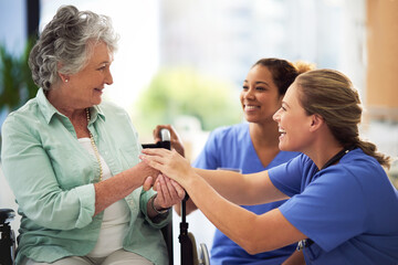 Shot of a smiling female doctor and nurse talking with a senior woman in a wheelchair