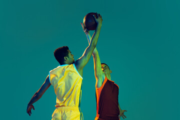 Portrait of two young men, professional basketball players in motion, training isolated over blue...