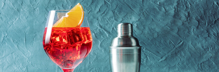 Aperol cocktail with an orange panorama, a side view with a shaker on a blue background, with a...