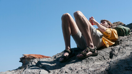 Hombre blanco tumbado en una roca costera mirando su móvil
