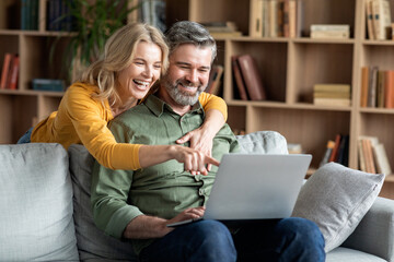 Joyful Middle Aged Spouses With Laptop Having Fun And Relaxing At Home