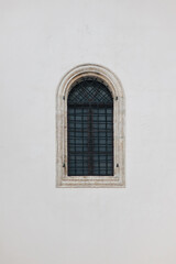 Antique old window with black iron bars framed on a light grey wall. The Jesuit Church in Lviv.
