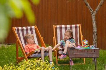 A little boy and a little girl lie on a sun lounger in the garden. Net sunny weather, two children...