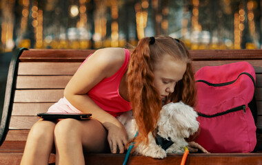 Girl bending over dog on park bench.