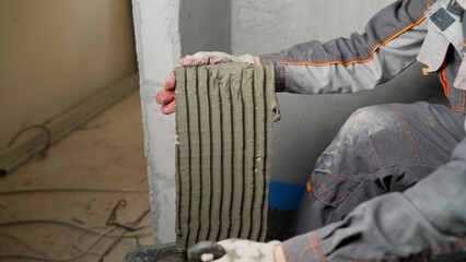 The master of laying tiles, takes a mixture for gluing finishing materials to the wall, close-up. Handyman installing ceramic tiles. Applying thinset mortar on a tile. Apply the adhesive, closeup.