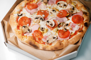 Italian pizza with salami and mushrooms and ham in a cardboard box. The process of making pizza. Street food cooking concept.