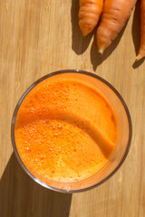 Raw carrots and fresh carrot juice on a wooden table