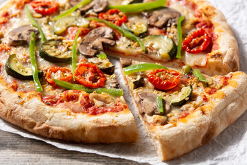 Vegetarian pizza with zucchini, tomato, peppers and mushrooms on wooden table. Close up