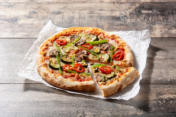 Vegetarian pizza with zucchini, tomato, peppers and mushrooms on wooden table	