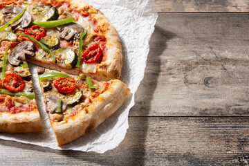 Vegetarian pizza with zucchini, tomato, peppers and mushrooms on wooden table. Copy space