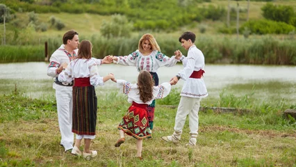 Foto op Canvas Happy family with kids in traditional romanian dress in a countryside, park. Father, mother, son and daughters dancing outside. © Dragosh