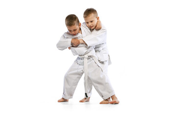 Dynamic portrait of two little boys, taekwondo or karate athletes wearing doboks training together...