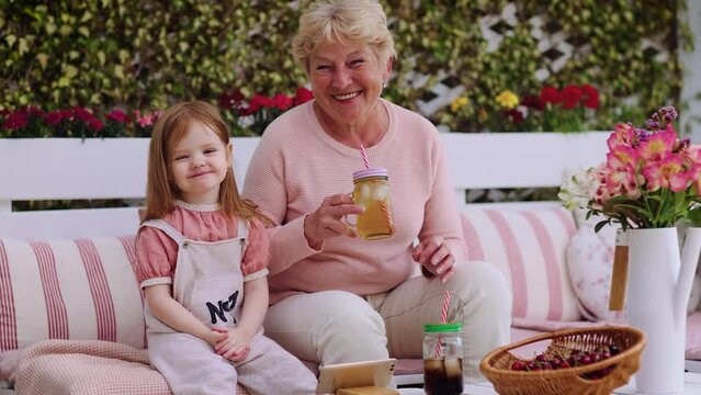 happy baby girl having fun with granny in summer garden, drinking chilling beverages