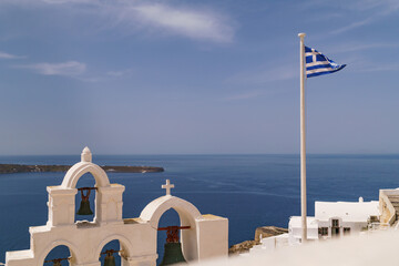 Classic and famous landmarks of the Greek island, Santorini. Greek national flag flying next to...