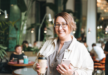 Adult brunette middle aged woman plus size body positive in casual clothes with paper cup of coffee...