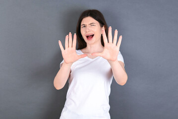 Dissatisfied young beautiful Caucasian woman wearing white T-shirt over studio grey wall frowns...