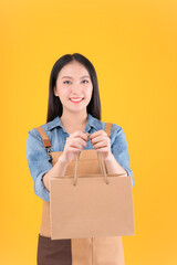 pretty asian female smile freelancer own shop show paper bags to customers buy products yellow background.