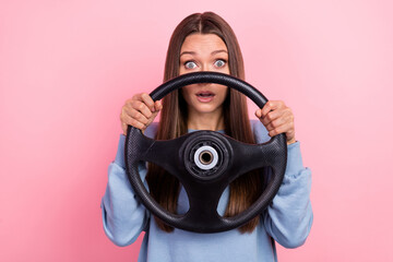 Portrait of attractive scared girl holding steering wheel hiding stare eyes isolated over pink...