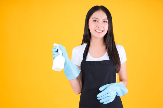 Attractive Asian Female Smile Wearing Black Apron Her Hands With Blue Rubber Gloves Holding A White Spray Bottle Poses Cleaning.