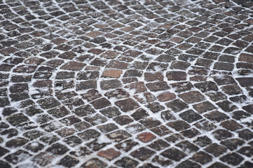 The vintage road is paved with old brown cobblestones. Paving stones with snow close-up. Winter...