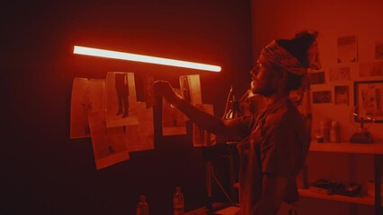 Indian male photographer using special tools and equipment while developing film and processing photos in darkroom