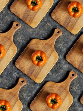 Pattern of orange sweet pepper on wooden cutting board on black concrete background. Rustic flatlay with spring vegetables.