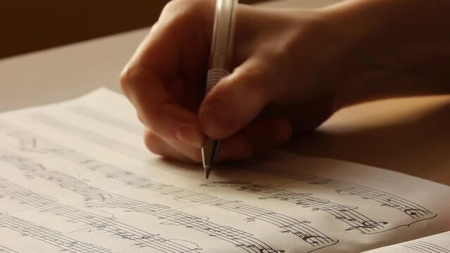 Handwritten notes and female hand holding a pen and writing notes, composing music, selective focus